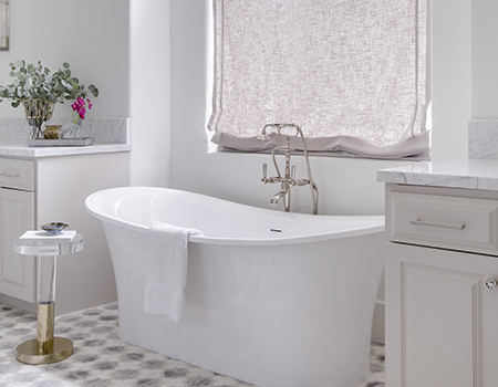 Detail of custom master bath with tile floors and oversized soaker tub under a window with a linen curtain. Dual vanities are on either side of the tub with brass fixtures in Houston, TX